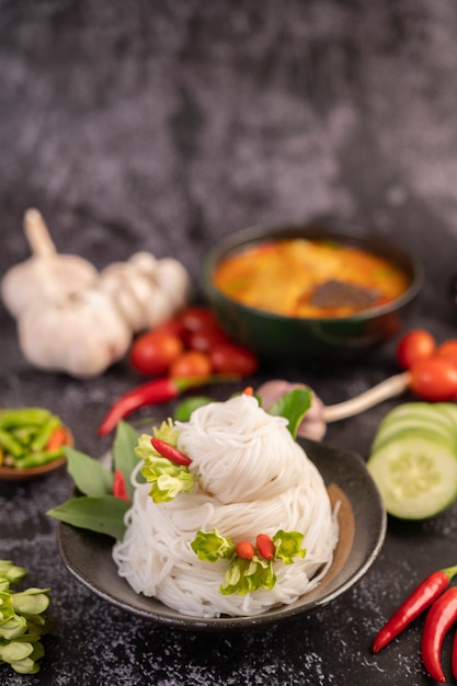 Chicken curry in a black cup with rice noodles.