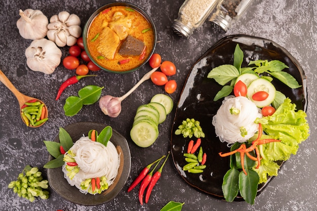 Chicken curry in a black cup with rice noodles.