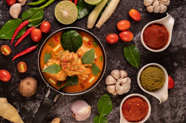 Chicken curry in a pan with lemongrass, kaffir lime leaves, tomatoes, lemon, and garlic