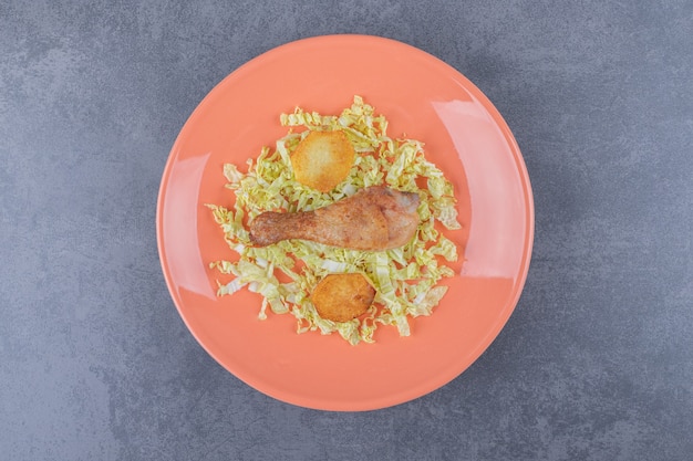 Chicken drumstick and fried potatoes on orange plate.