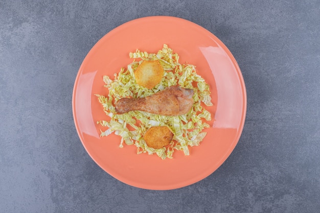 Куриная голень и жареный картофель на оранжевой тарелке.