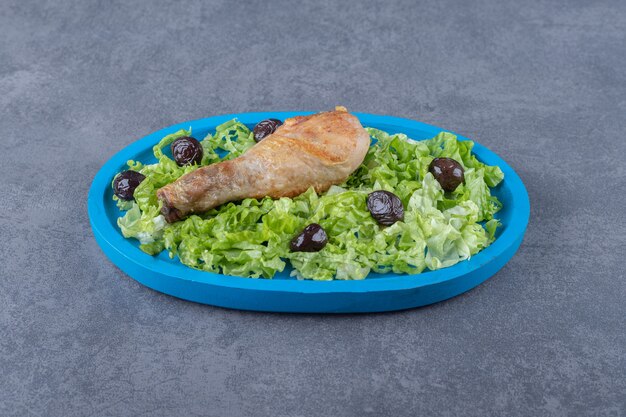 Chicken drumstick, olives and lettuce on blue plate.