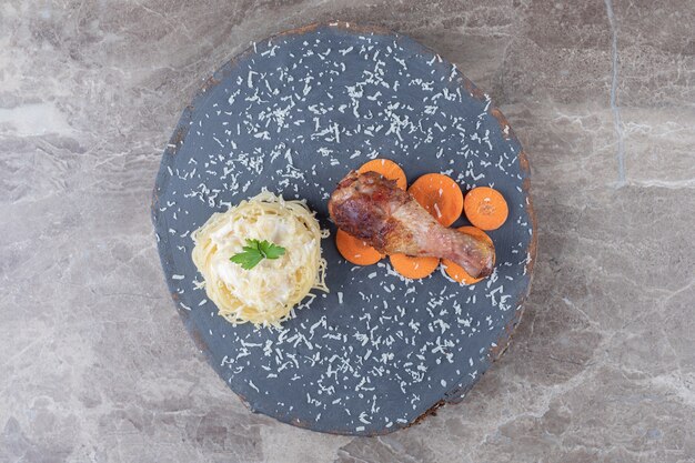Chicken drumstick on the sliced carrot next to spaghetti on the wooden board , on the marble.