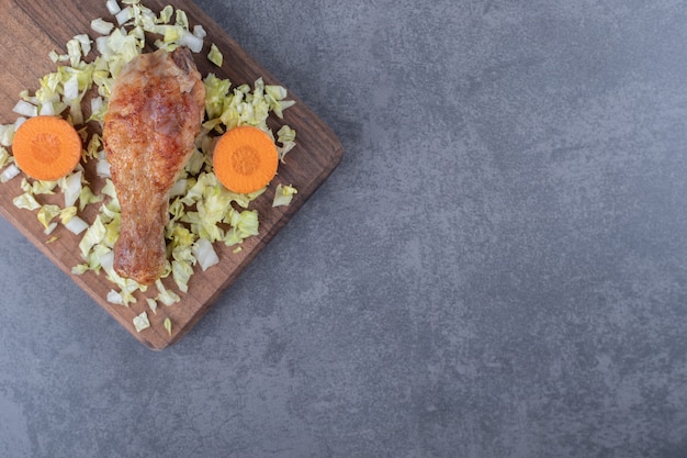 Chicken drumstick and sliced vegetables on wooden board.