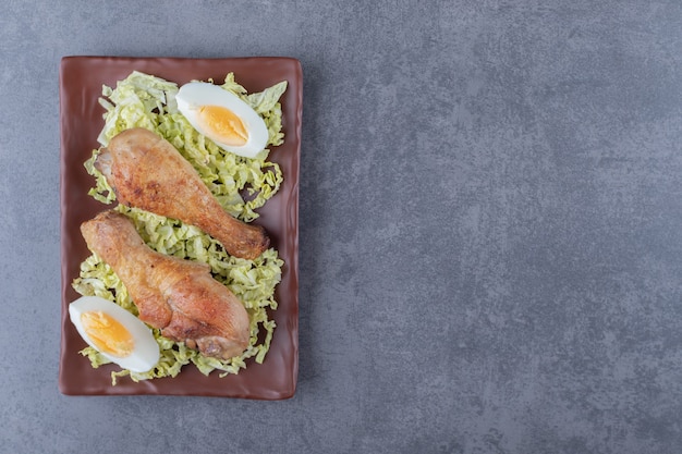 Chicken drumsticks and boiled eggs on brown plate.