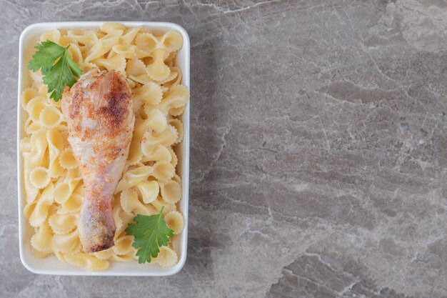 Chicken drumsticks over pasta in the bowl , on the marble background.