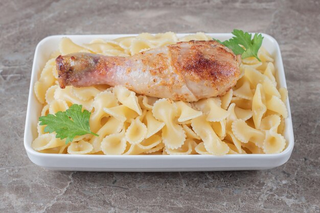 Chicken drumsticks over pasta in the bowl , on the marble surface.