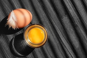 chicken egg and yolk with a glass on a dark wooden table with copy space sunlight on a wooden table and shadow stripes