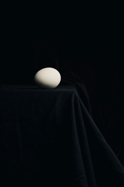 Chicken egg on edge of table between blackness