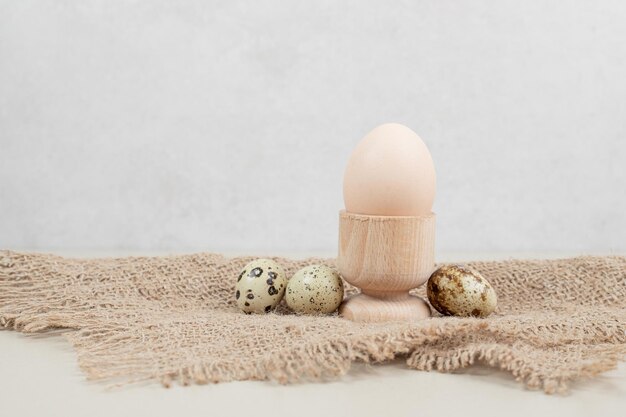 Chicken egg in egg cup with quail eggs on sackcloth .