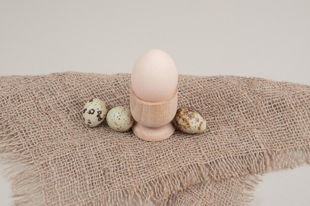 Chicken egg in egg cup with quail eggs on sackcloth .