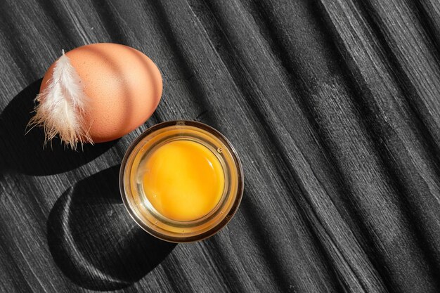 Chicken egg and yolk with a glass on a dark wooden table with copy space sunlight on a wooden table and shadow stripes