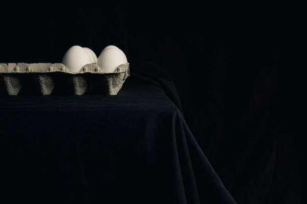 Free photo chicken eggs in container on edge of table between blackness