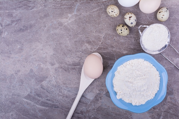 Free photo chicken eggs and a cup of all purpose flour on table.