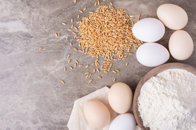 Chicken eggs and a cup of all purpose flour on table.