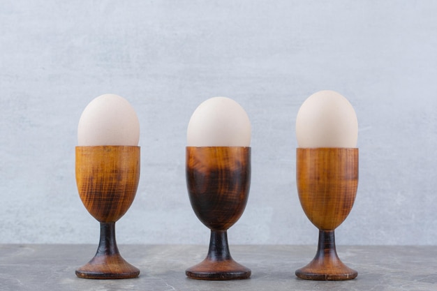 Куриные яйца в яичных чашках на мраморном фоне. Фото высокого качества