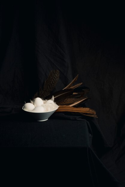 Chicken eggs between feathers in bowl near big quills