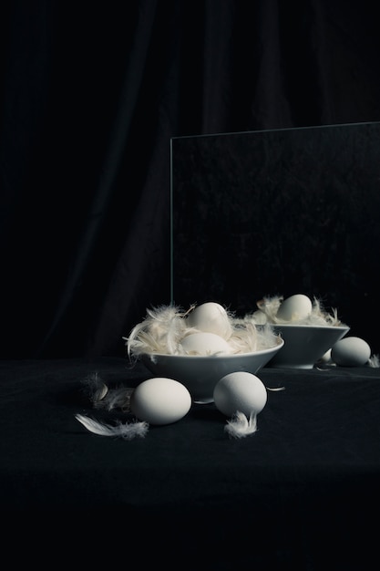 Chicken eggs between feathers in bowl near mirror