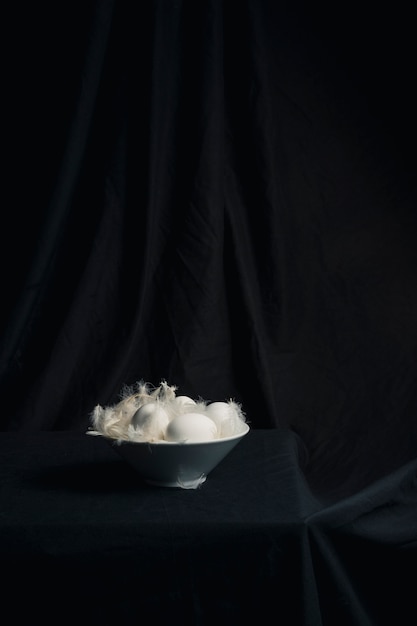 Chicken eggs between feathers in bowl on table 