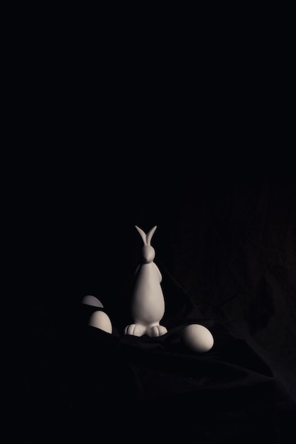 Free photo chicken eggs and figure of rabbit between dark material