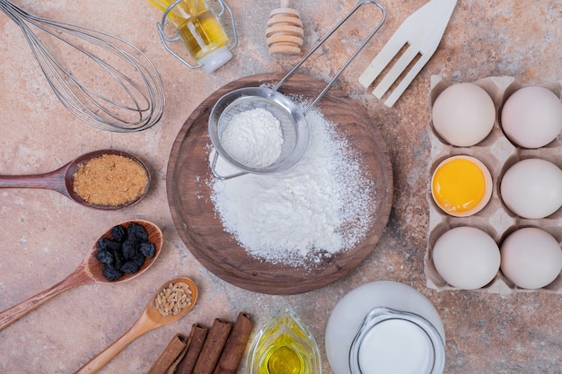 Chicken eggs, milk, flour and spices on marble surface.