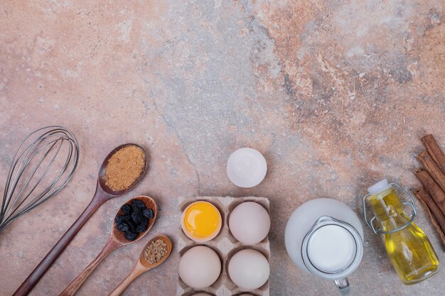 Chicken eggs, milk, oil and spices on marble surface.