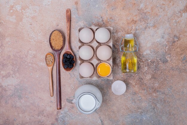 Chicken eggs, milk, oil and spices on marble surface.