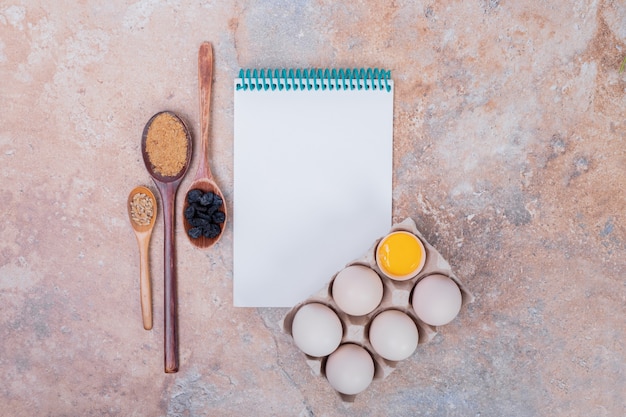 Chicken eggs and notebook on marble surface.