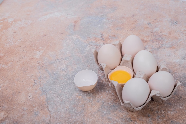 Chicken eggs in paper container on marble surface.