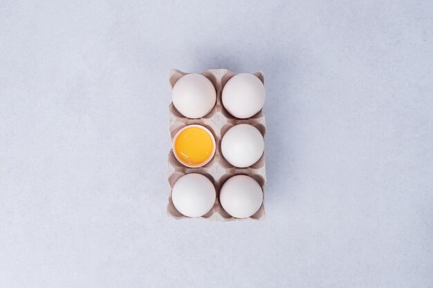 Chicken eggs in paper container on white surface.