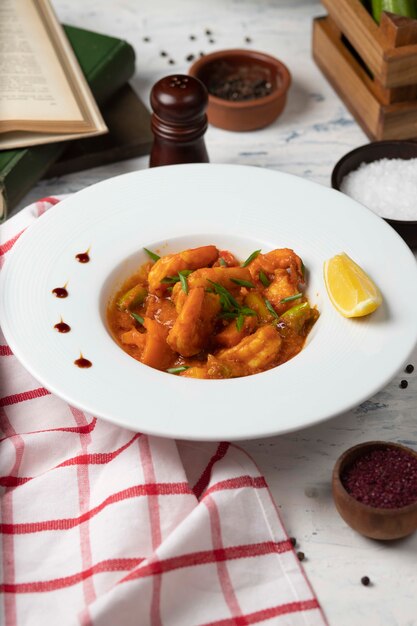 Chicken feet stew in tomato sauce in white bowl with vegetables and lemon. 