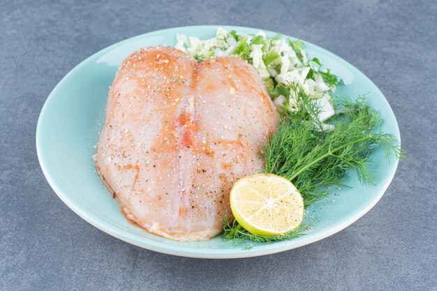 Chicken fillet and lemon on blue plate.