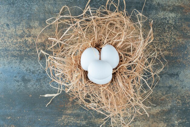 Chicken fresh white eggs lying in hay on marble background