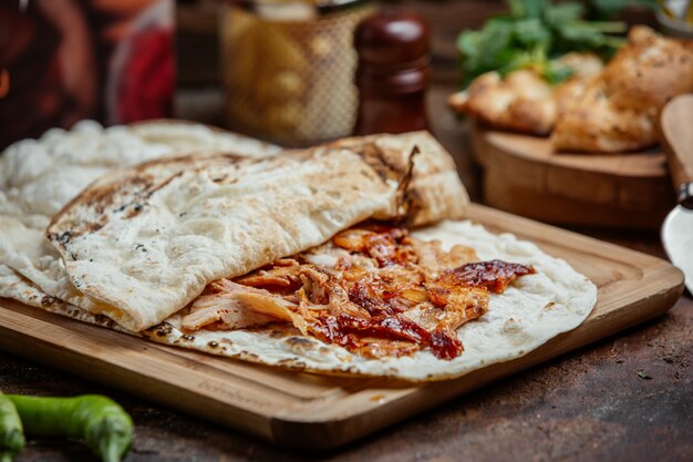 chicken kebab doner with ketchup inside of flatbread on wooden board