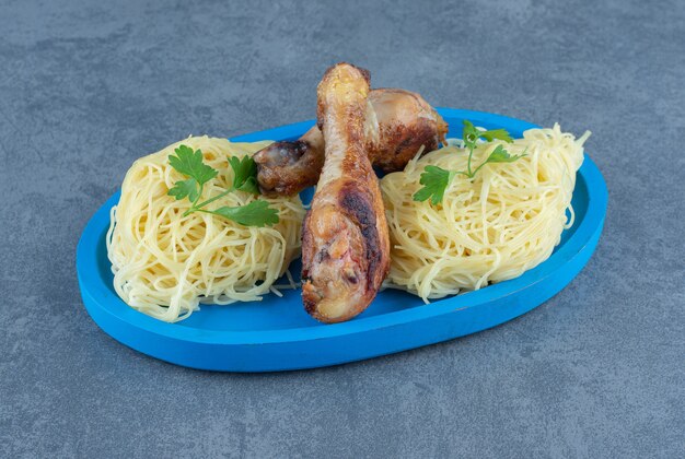 Chicken legs and spaghetti on blue plate.