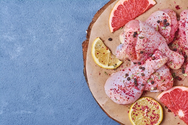 Chicken legs with fruits on a wooden board on blue