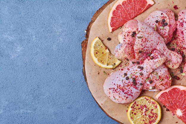 Chicken legs with fruits on a wooden board on blue