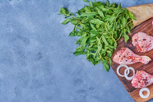 Free photo chicken legs with herbs on a wooden board on blue