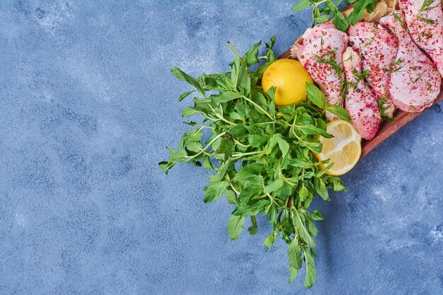 Chicken legs with herbs on a wooden board on blue