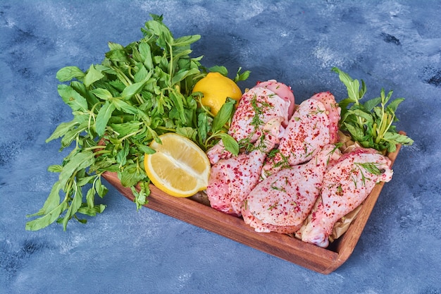 Free photo chicken legs with herbs on a wooden board on blue