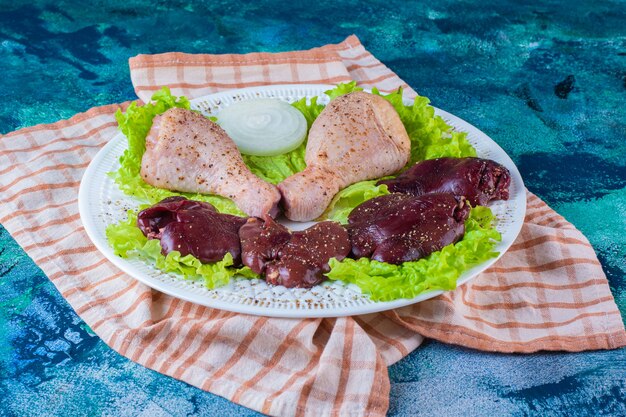 Куриная печень, листья салата и куриная голень на тарелке на кухонном полотенце