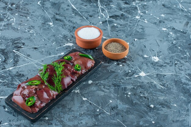 Chicken livers on a board next to spice bowls, on the blue background.