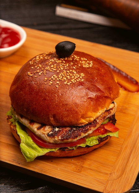 Foto gratuita hamburger di carne di pollo con fette di pomodoro e lattuga servito con ketchup e maionese sul bordo di legno