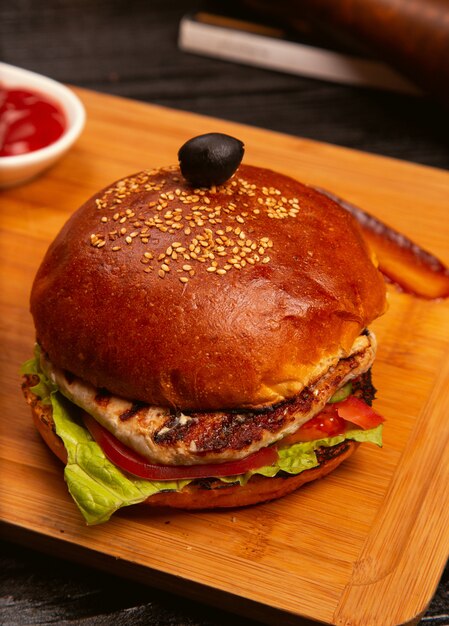 Chicken meat burger with tomato slices and lettuce served with , ketchup and mayonnaise on wooden board