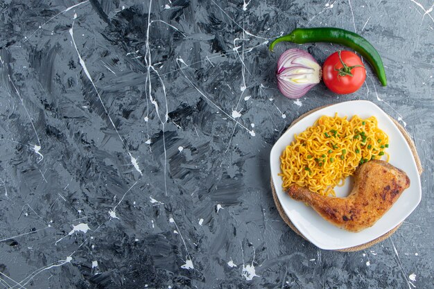 Chicken meat and noodle on a plate on a trivet next to vegetables , on the marble background. 