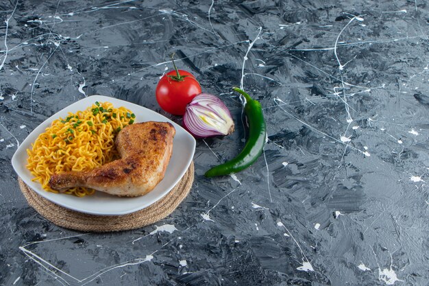 Chicken meat and noodle on a plate on a trivet next to vegetables , on the marble background. 