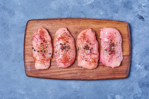 Куриное мясо со специями на деревянной доске на синем