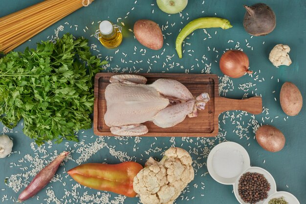 Chicken meat on a wooden board with pasta and vegetables around.