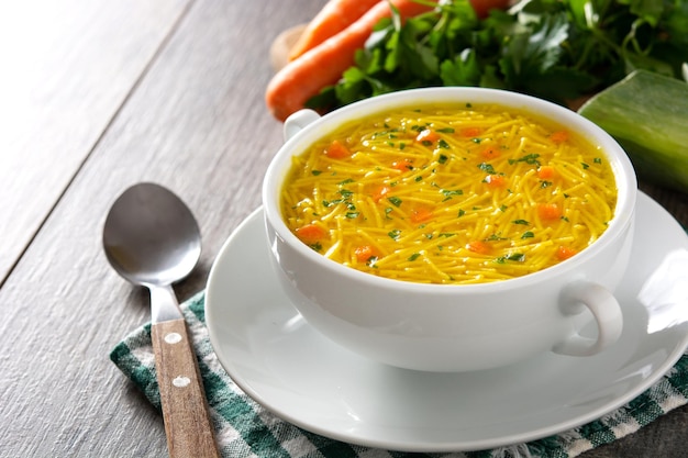 Chicken noodle soup in white bowl on wooden table