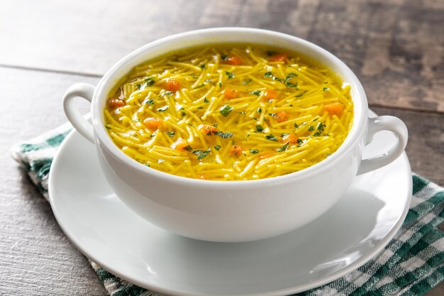 Chicken noodle soup in white bowl on wooden table